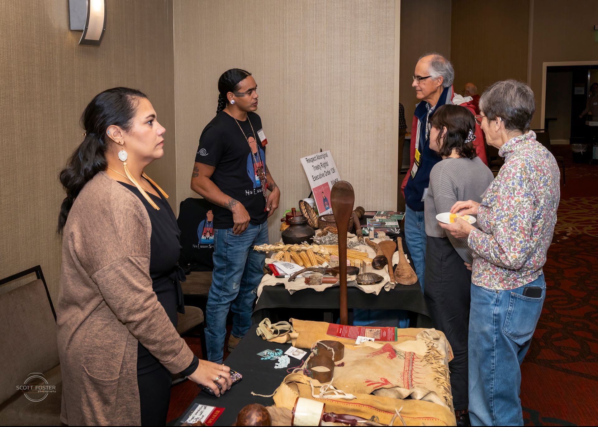 People at a display booth with artifacts and talking. Indoor setting, various skin tones, items on the table.