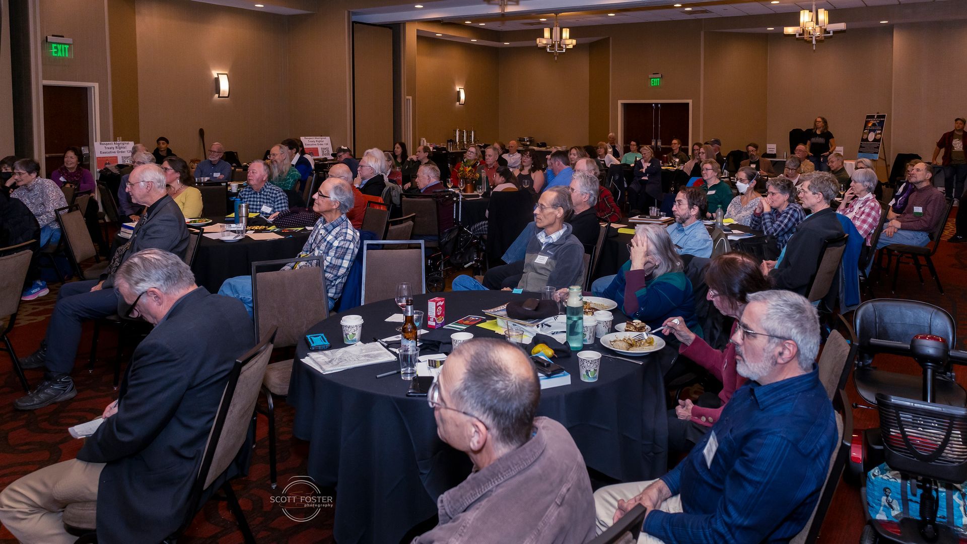 People at tables in a large conference room, listening to a presentation.