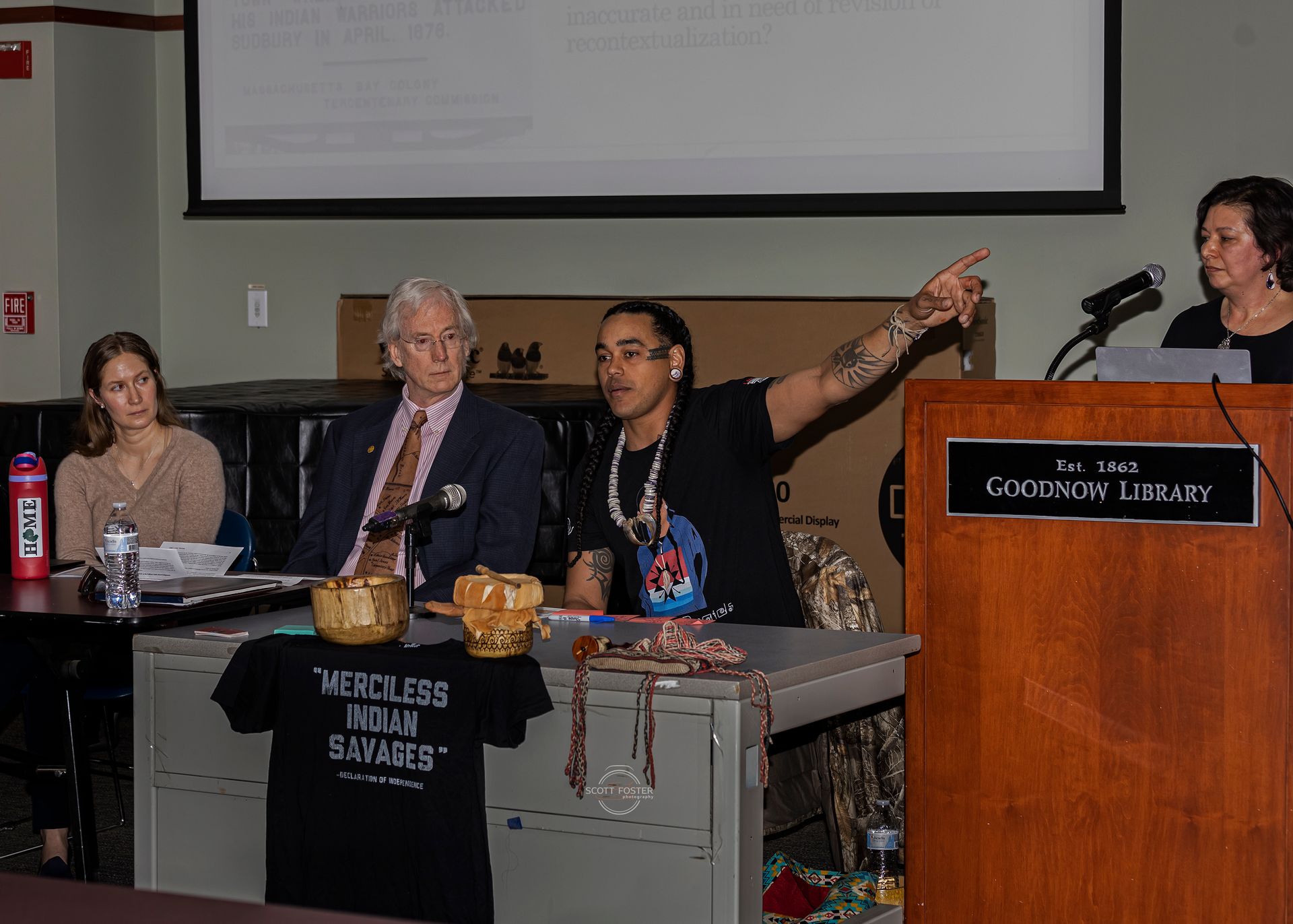 Panel discussion at a podium in a library, man pointing, others listening.