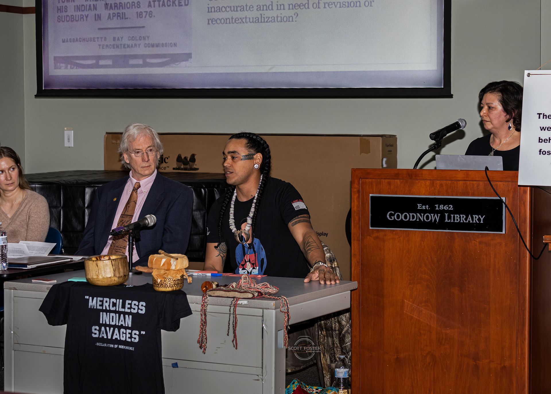 Panel at a podium, discussing; display with text, Native American cultural items, and a 