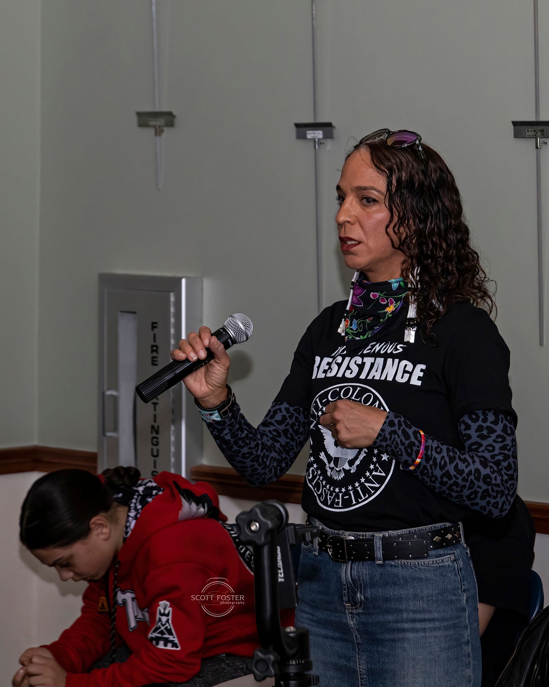 Woman speaks into a microphone, wearing a t-shirt that says 