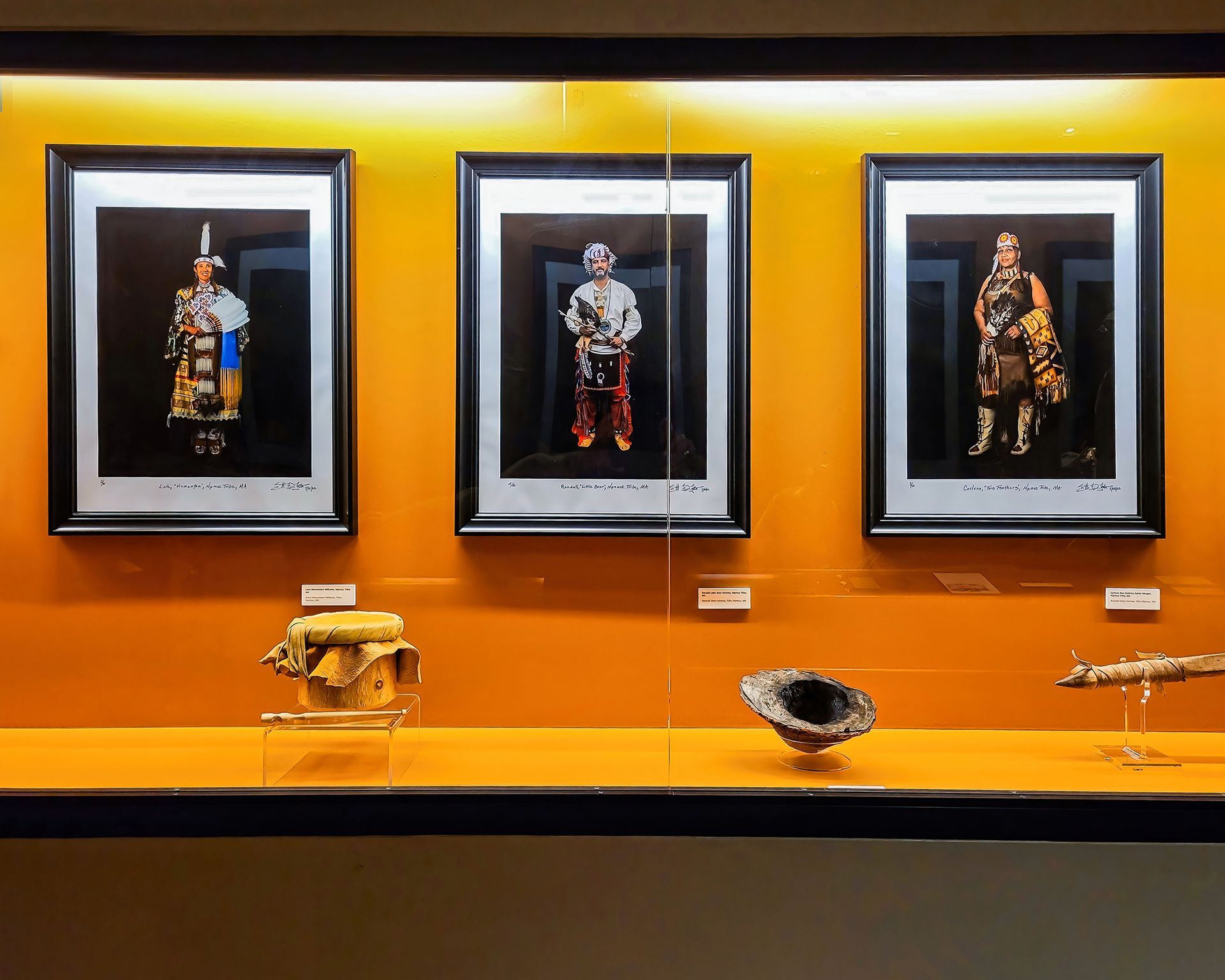 Three framed portraits of Native American figures in a museum display with artifacts below.
