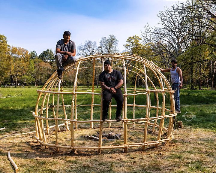 Three people standing near a wooden framework of a dome-shaped structure outdoors.