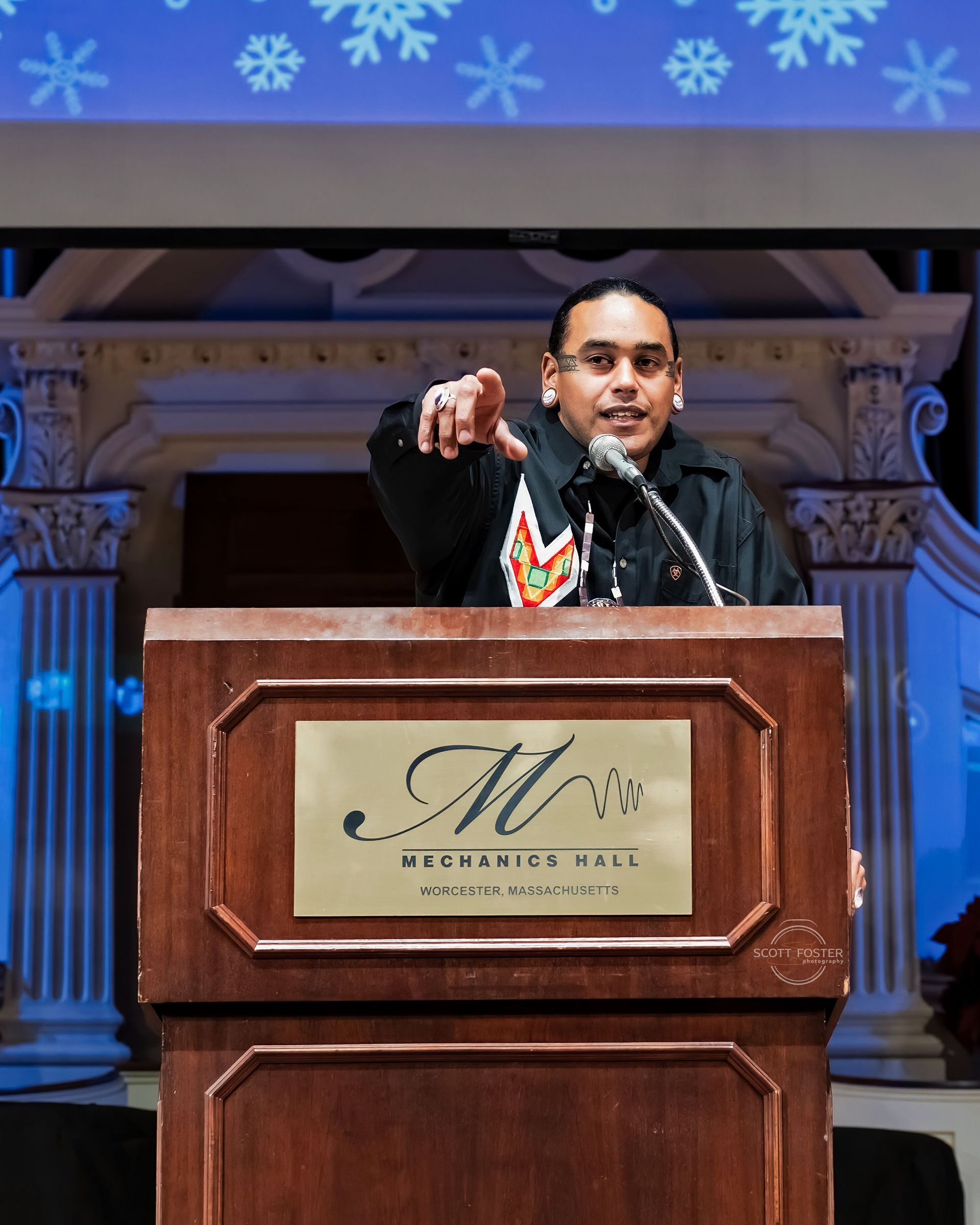Man speaking at a podium, pointing forward. 