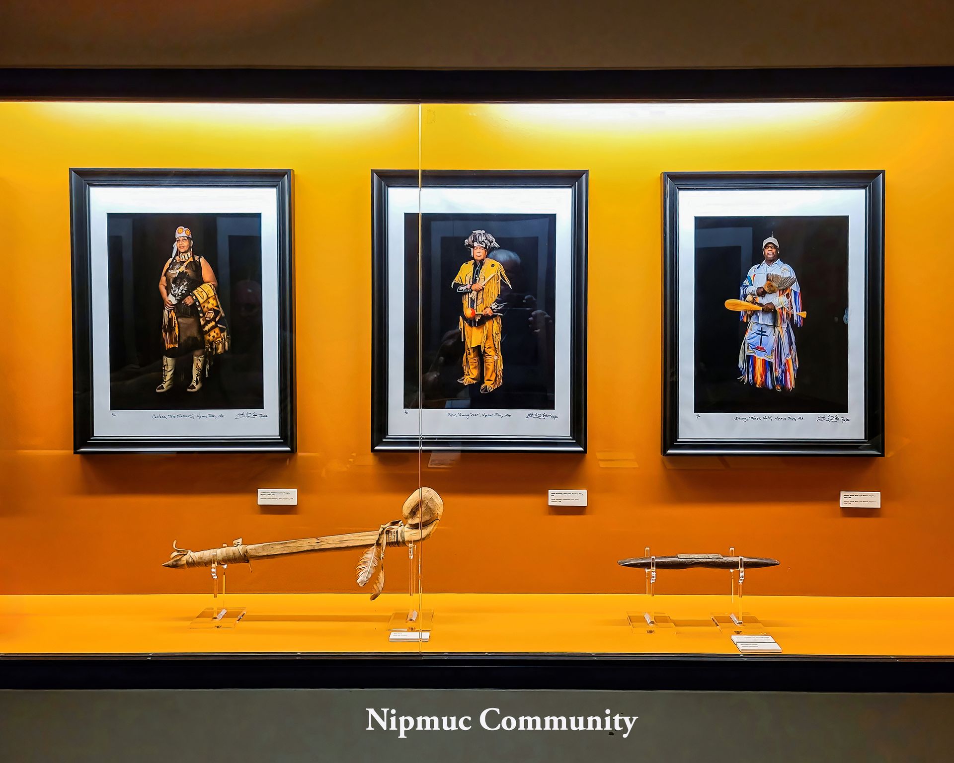 Three framed portraits of figures in colorful attire, displayed above artifacts in a museum case.