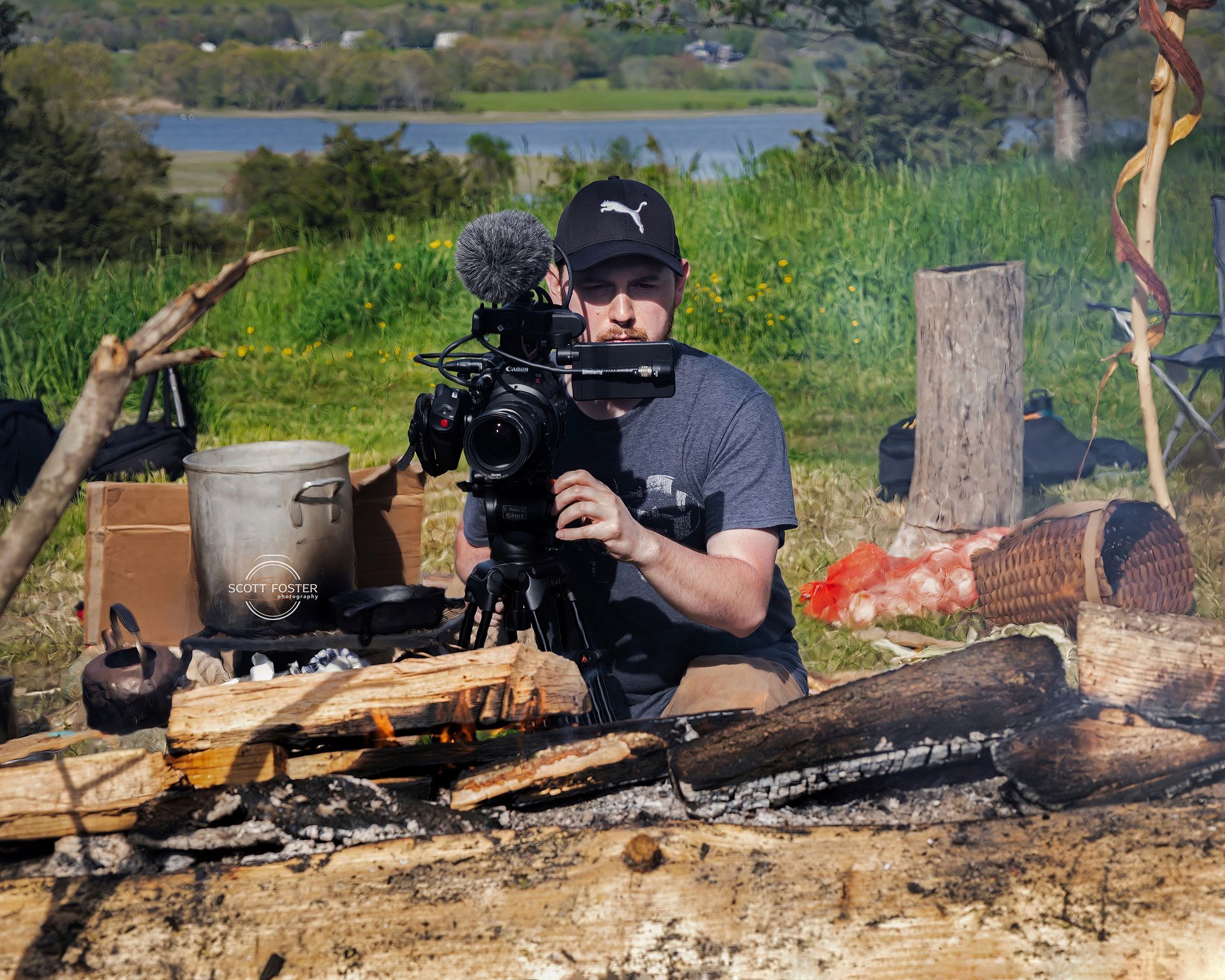 A person filming with a camera over a campfire; outdoor setting.