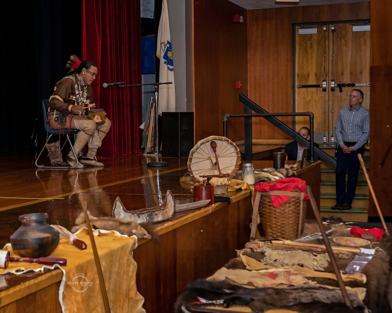 Person playing a drum on stage, historical artifacts displayed, another person standing.