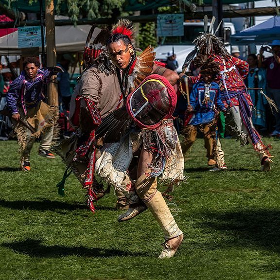 Native American dancers in colorful regalia perform on a grassy field.