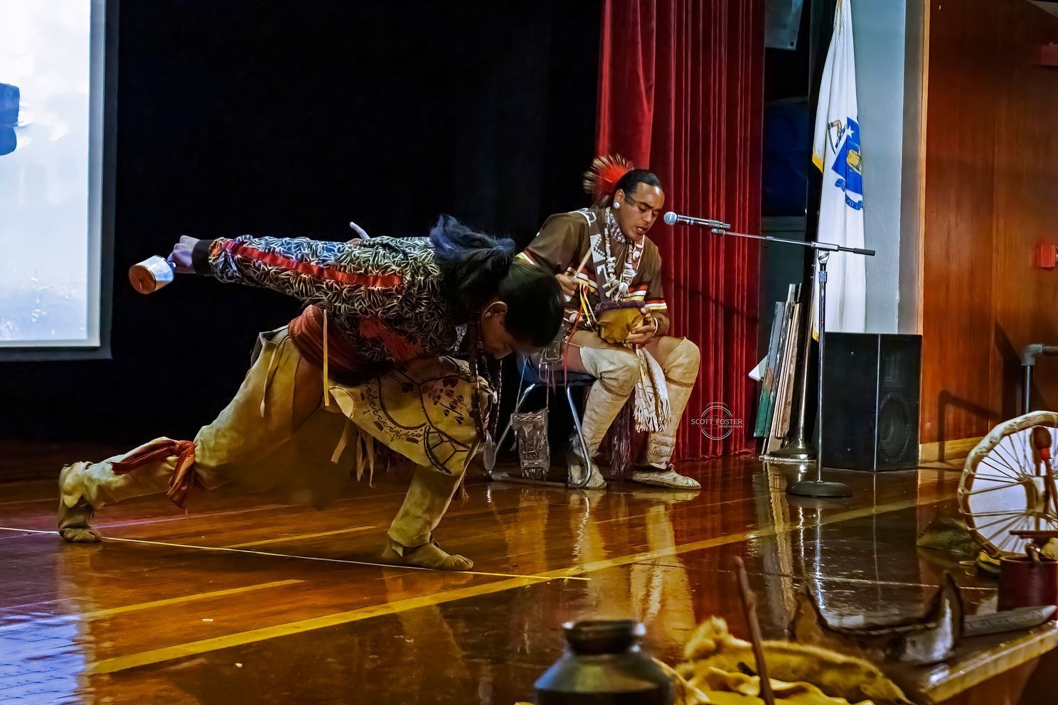 Two performers on stage: one dancing, the other singing and playing percussion.