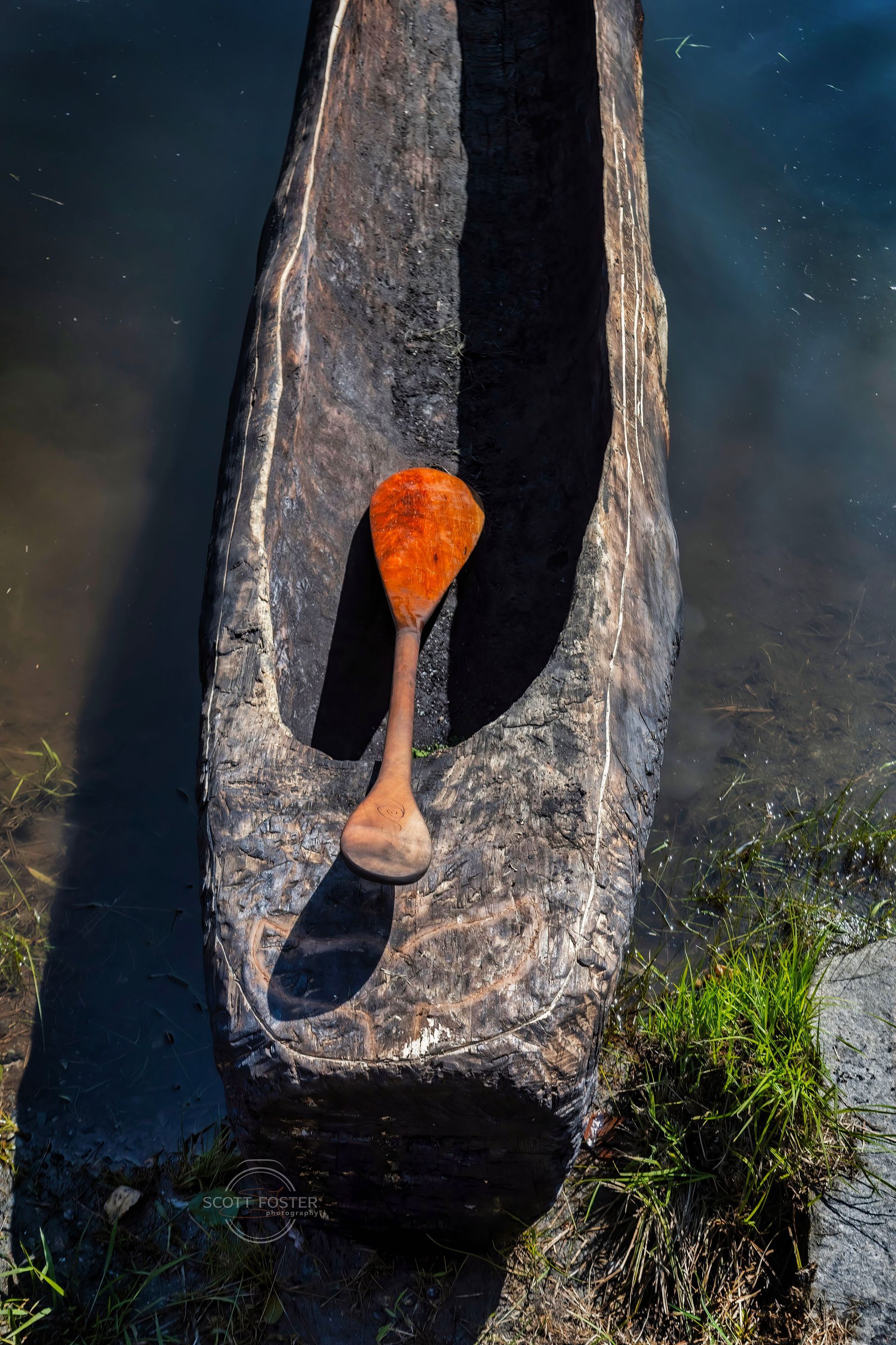 Wooden canoe with an orange scoop, in water.