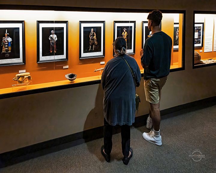 Two people view framed displays of figures and artifacts in a museum exhibit.