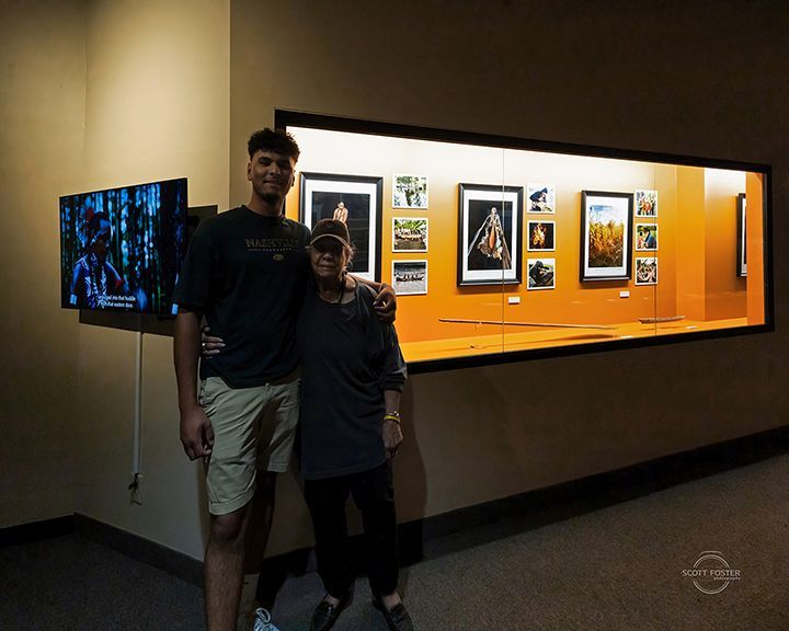 Person with arm around another person, standing in front of framed artwork.