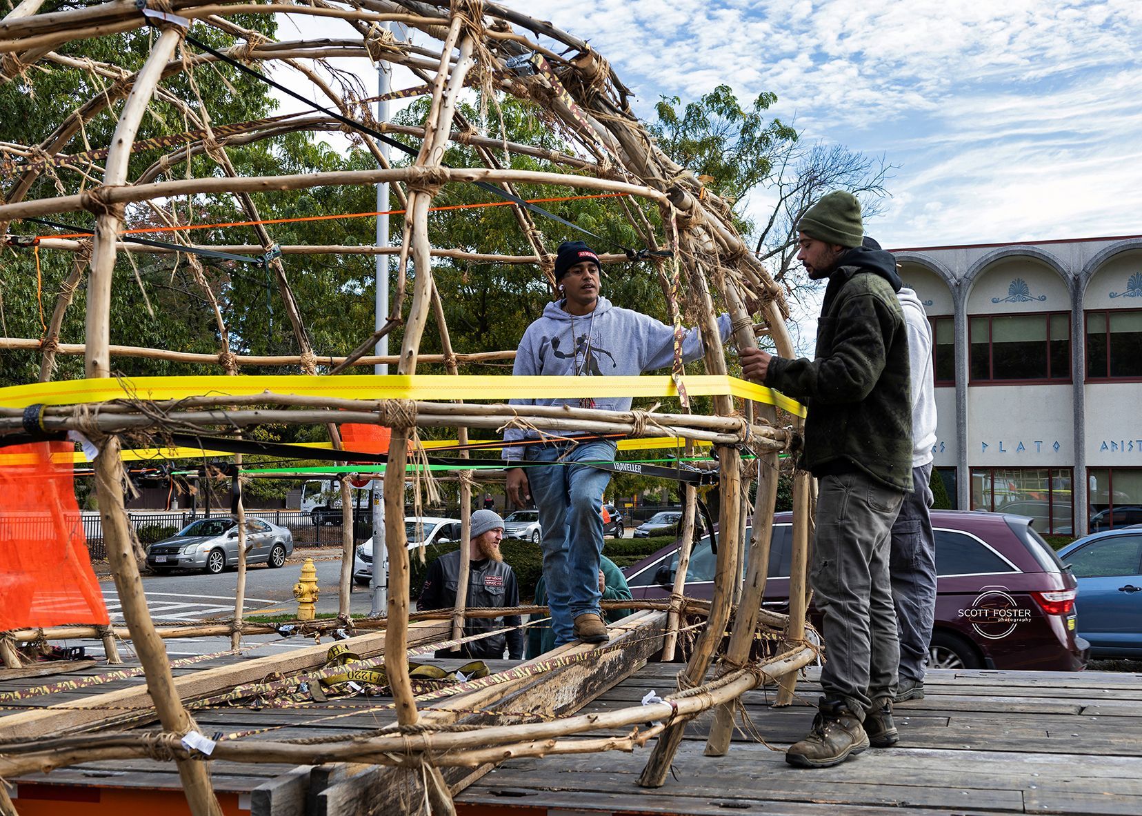 People building a wooden dome structure outdoors on a trailer near a road.