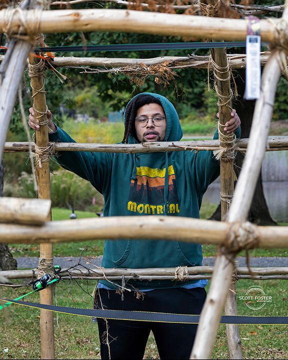 Person in hoodie framed by a wooden structure outdoors.
