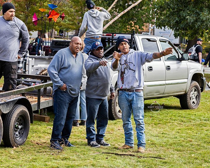 Men pointing, directing near a truck and trailer on a grassy area, likely filming outdoors.
