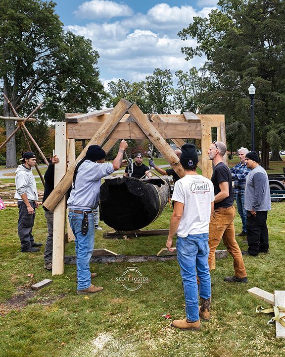 Group of people constructing a wooden structure around a large, dark, rounded object on grass.