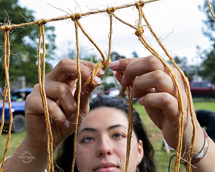 Woman knotting natural fiber rope to create a grid structure outdoors.