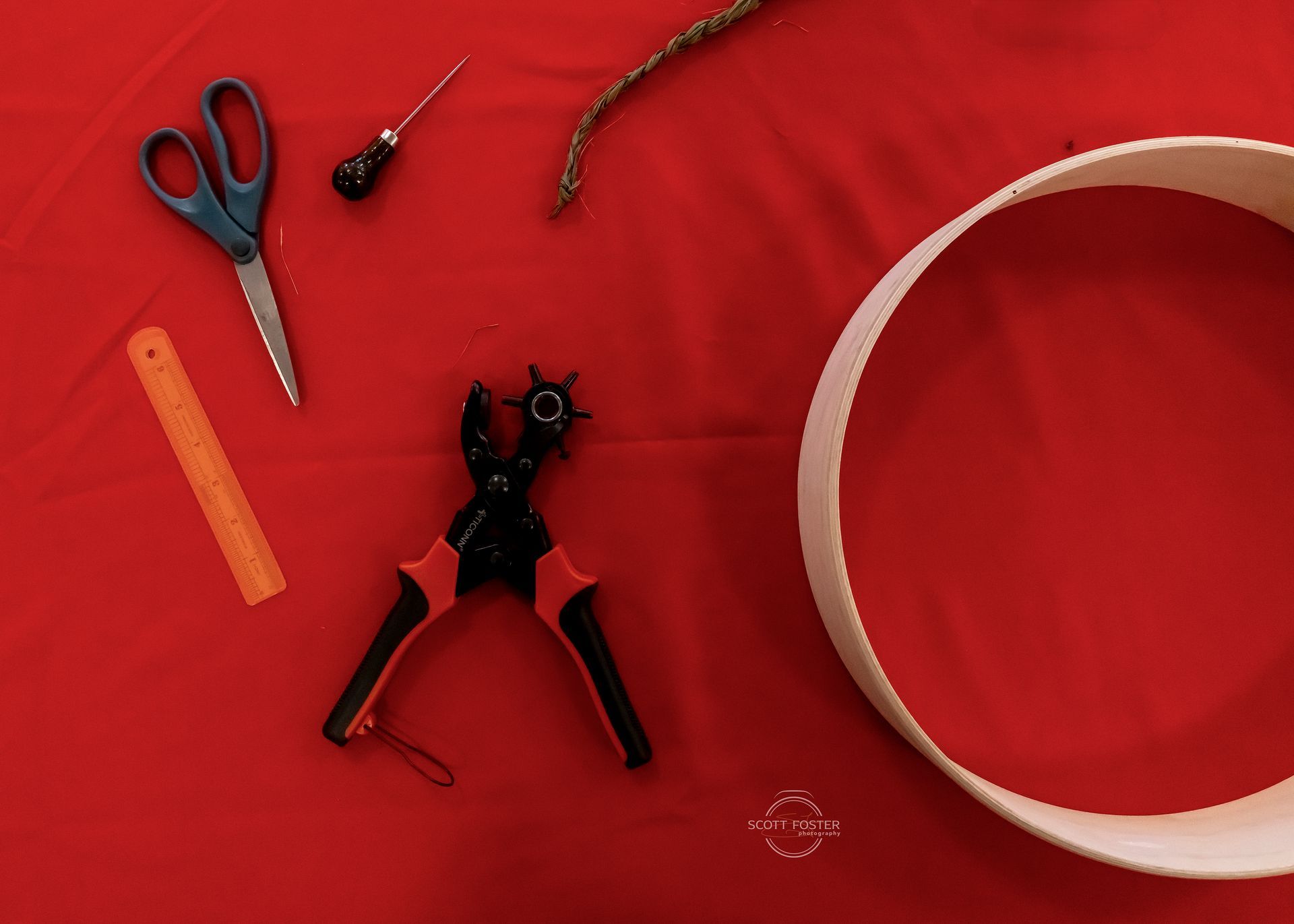Tools laid out on red fabric: scissors, punch pliers, ruler, awl, and a craft ring.