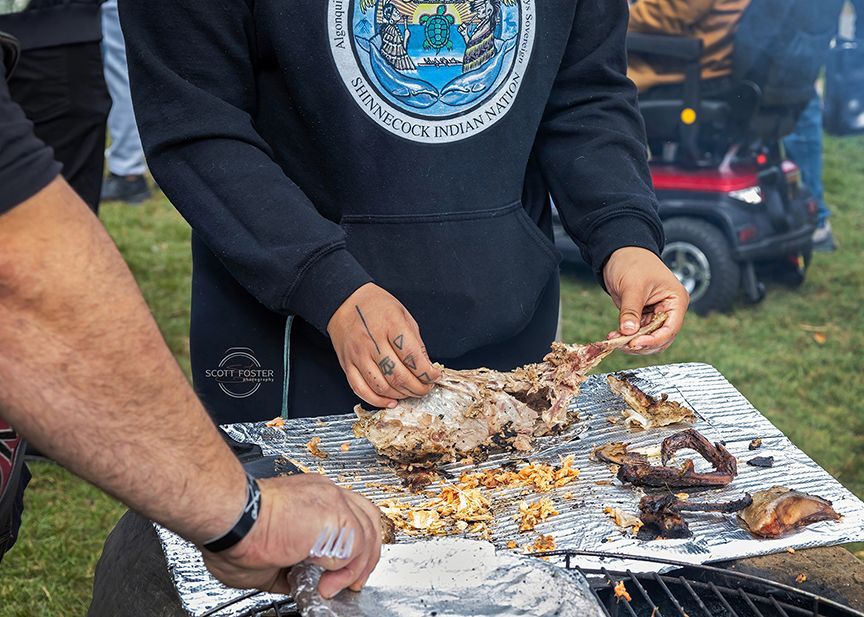 Two people preparing cooked food on a foil-covered surface outdoors; one person wearing a black hoodie.