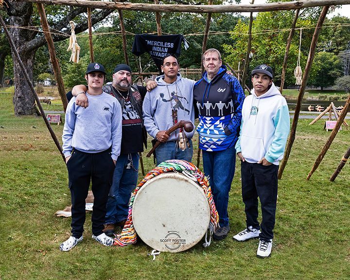 Five people pose with a large drum and wooden structure outdoors.