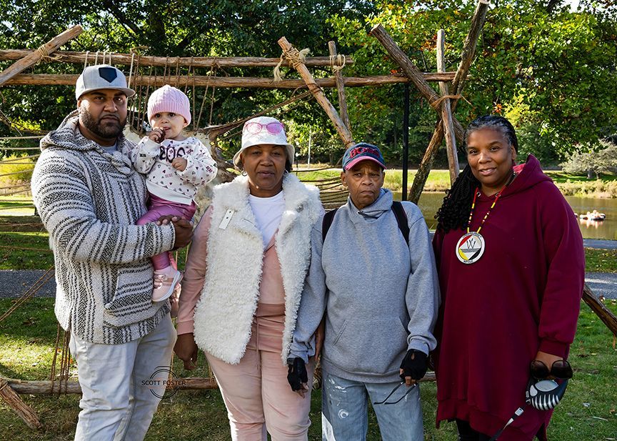Group of five people pose outside with wooden structure and a pond.