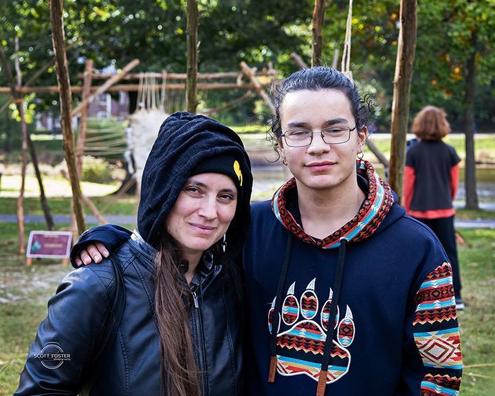 Woman in black jacket and beanie, arm around a young person in a hoodie with a bear paw design. Outdoors.