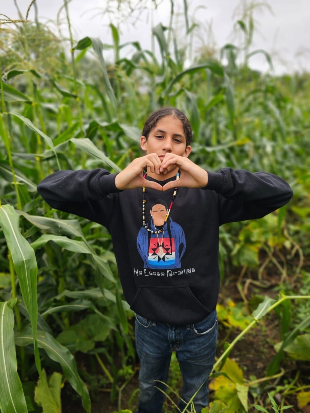 Person in black hoodie forming a heart with hands in a field of corn.