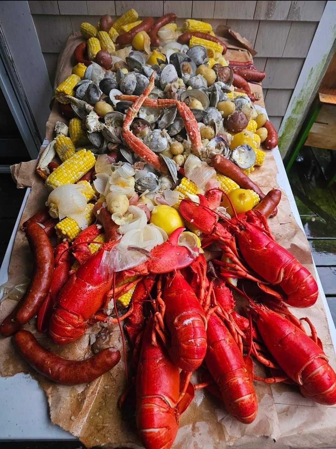 Seafood boil on a table: lobster, clams, crab legs, sausage, corn, potatoes, all steamed and ready to eat.