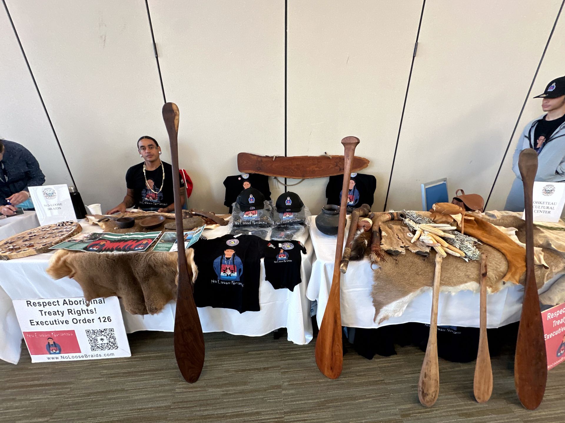 A vendor booth with paddles and merchandise. A person stands behind the table.