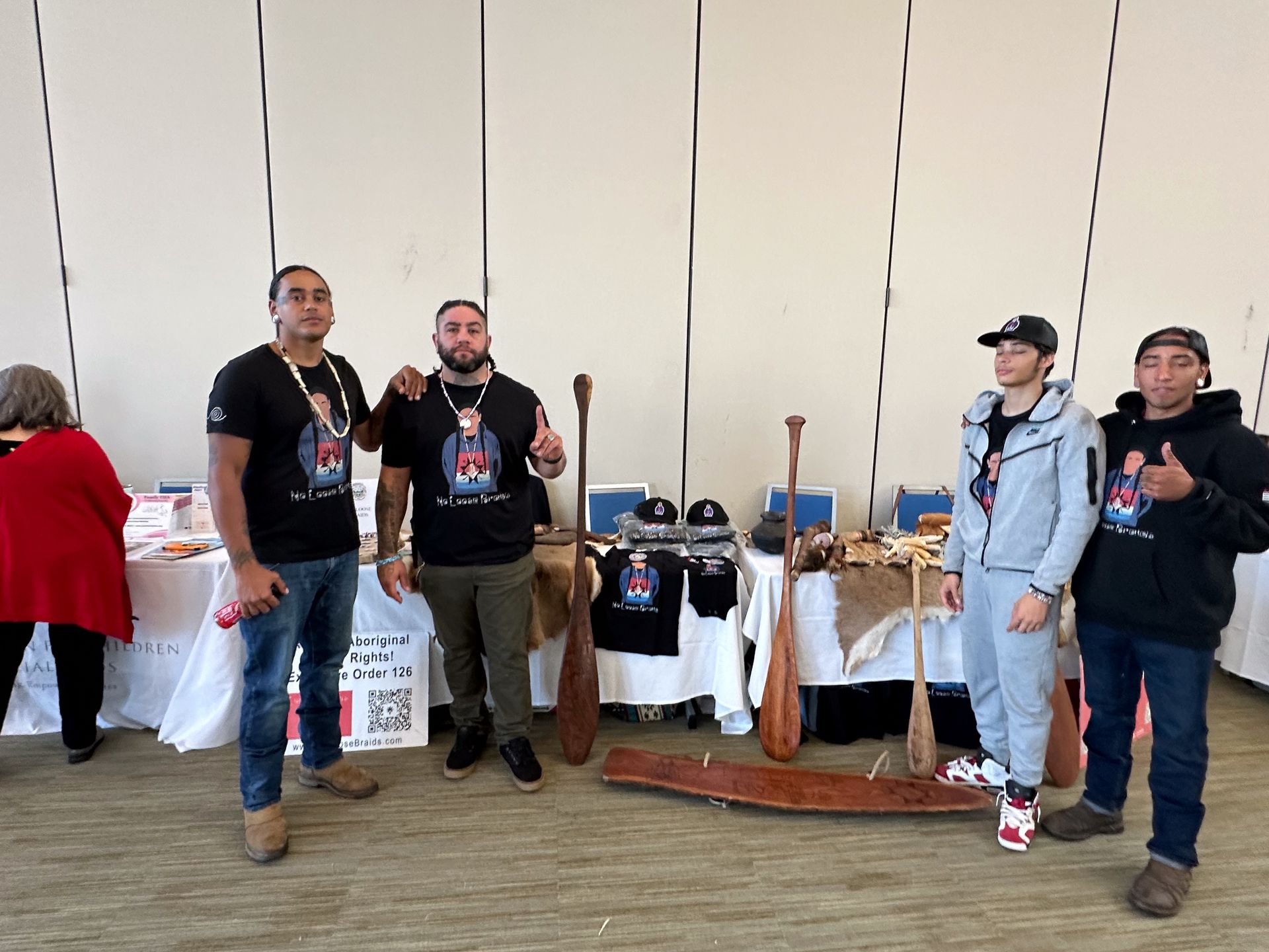 Four people pose at a table with paddles and merchandise. A woman in red is to the left.