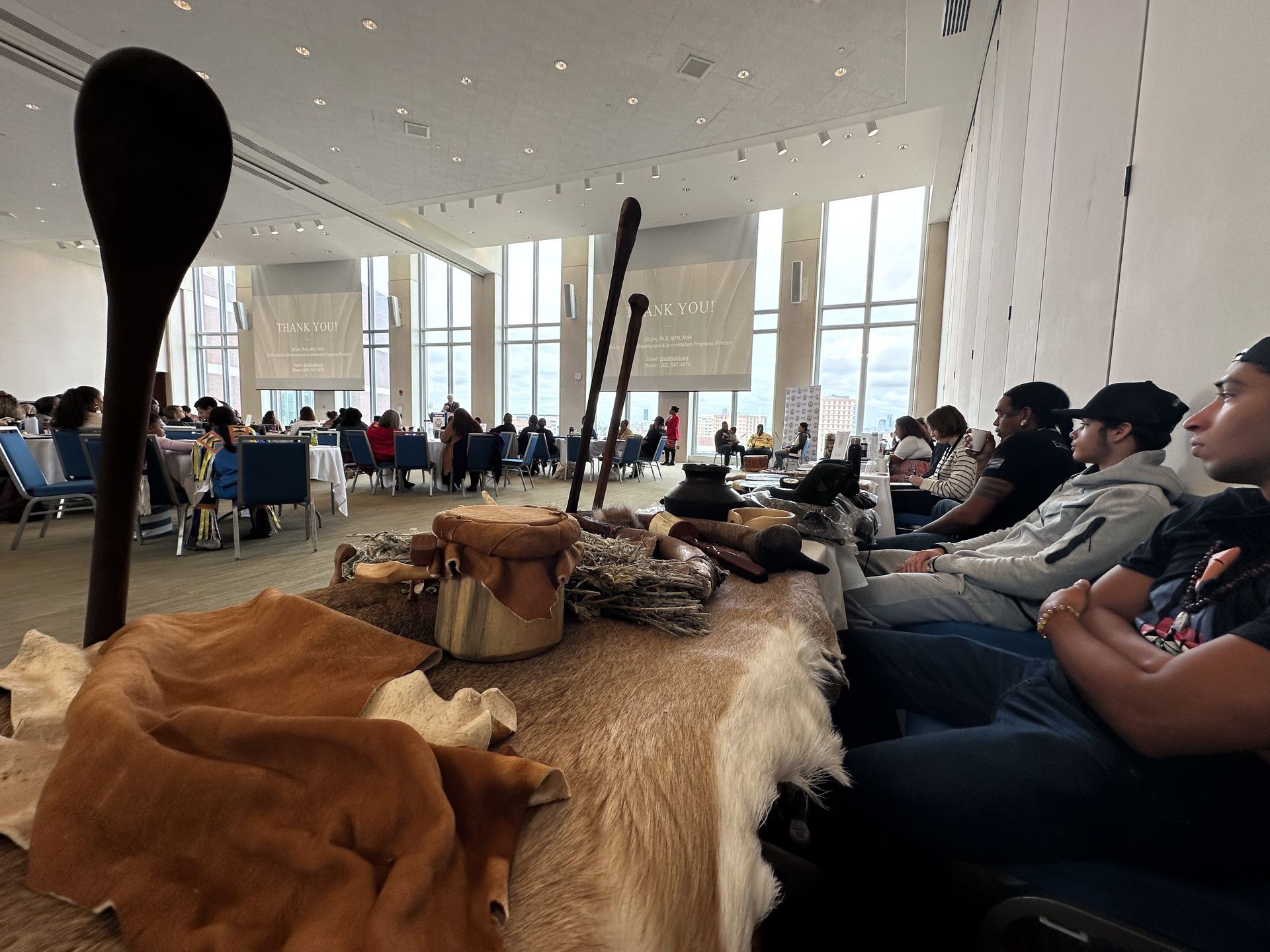 Conference room with table display of artifacts; people seated, listening to presentation.