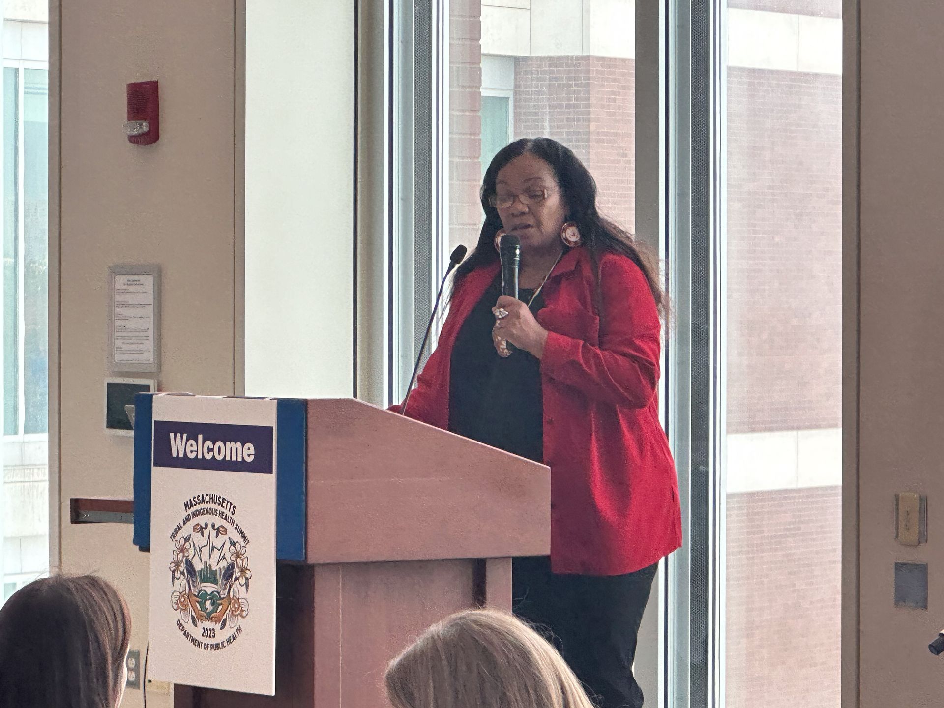 Woman in red blazer speaks at a podium with 