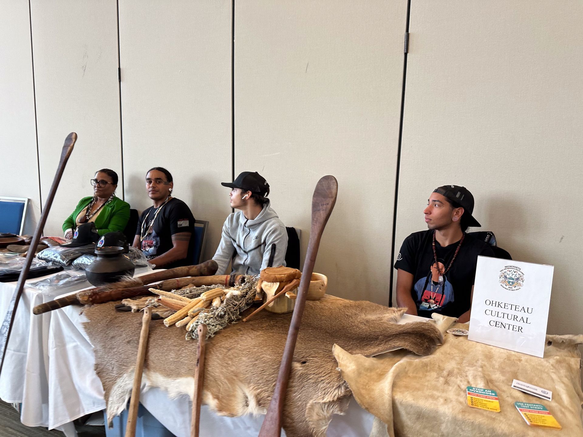 People at a table with cultural items, seated indoors. A sign reads, “Cultural Center.”