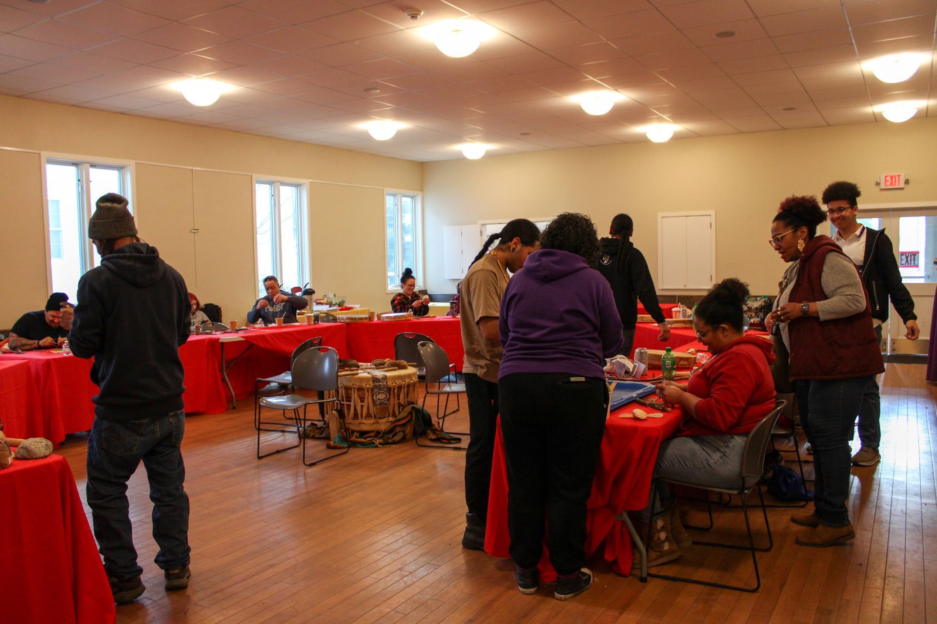 People seated around tables in a room, red tablecloths, a presentation screen.
