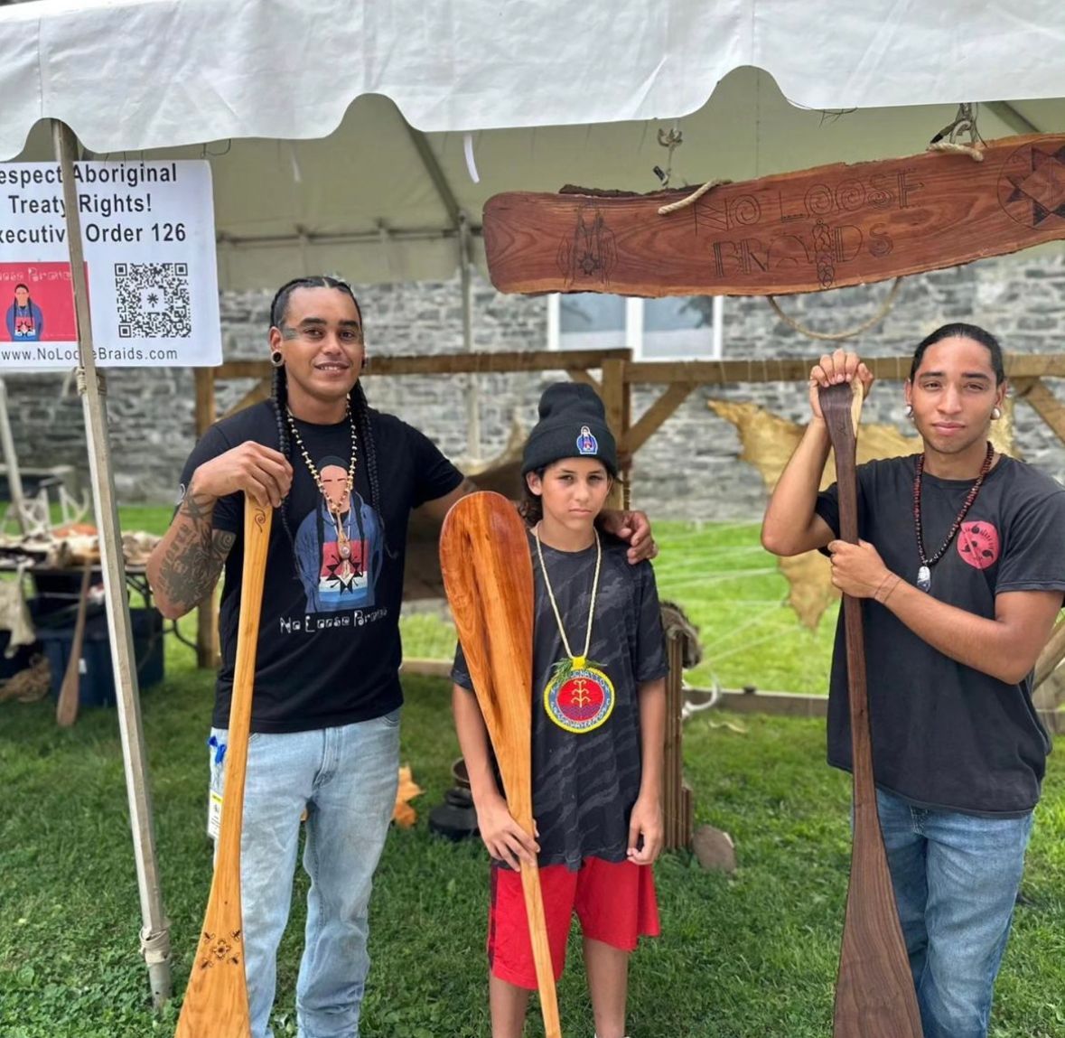 Three people with paddles stand near a tent. Two adults and a child. Sign visible: 