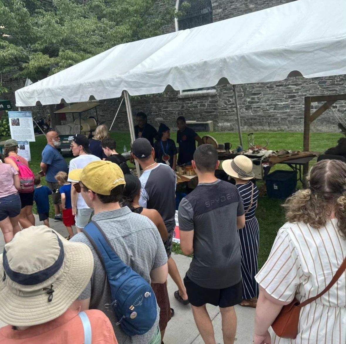 A crowd of people at an outdoor event under a white tent; displays visible.