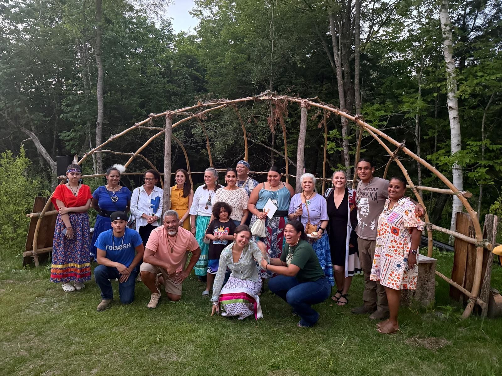 Group of people pose in front of a wooden archway in a grassy outdoor setting.
