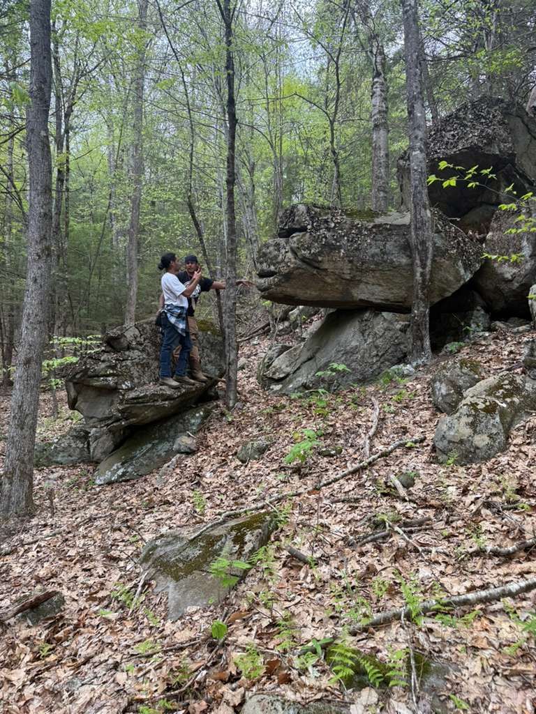 Two people standing on rocks in a wooded area, one holding a camera, shooting.