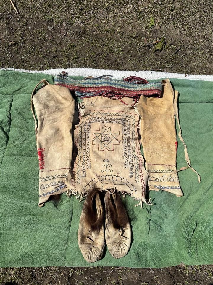Set of antique Native American clothing and accessories laid out on a green surface. Includes bag, shoes, and gloves.
