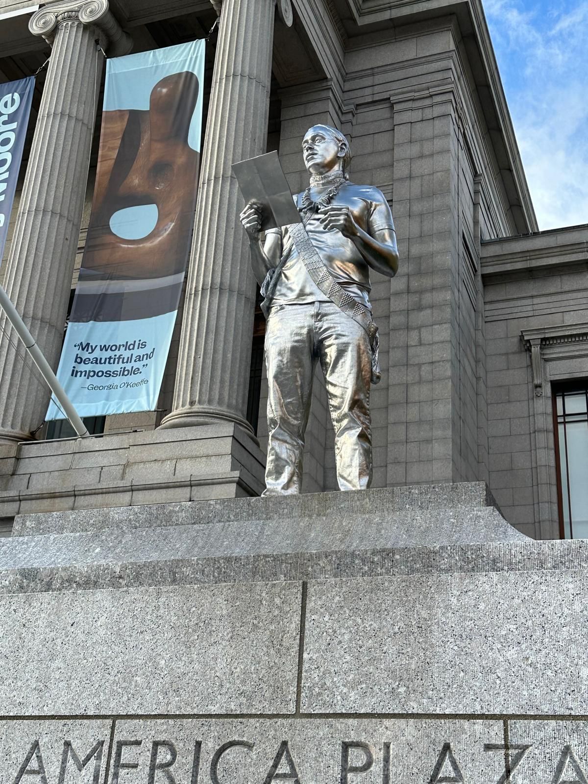 Silver statue of a man holding paper, standing on granite steps labeled 
