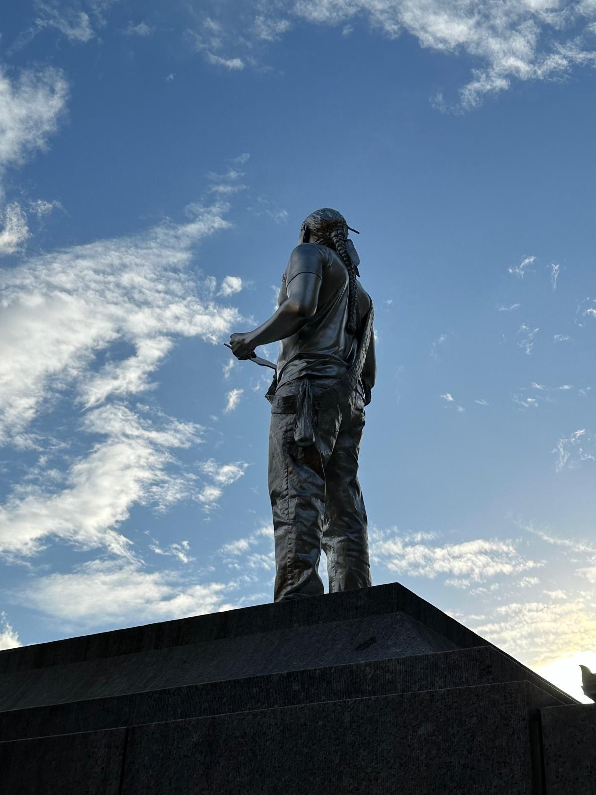 Statue of a person, holding object, set against a blue sky with clouds.