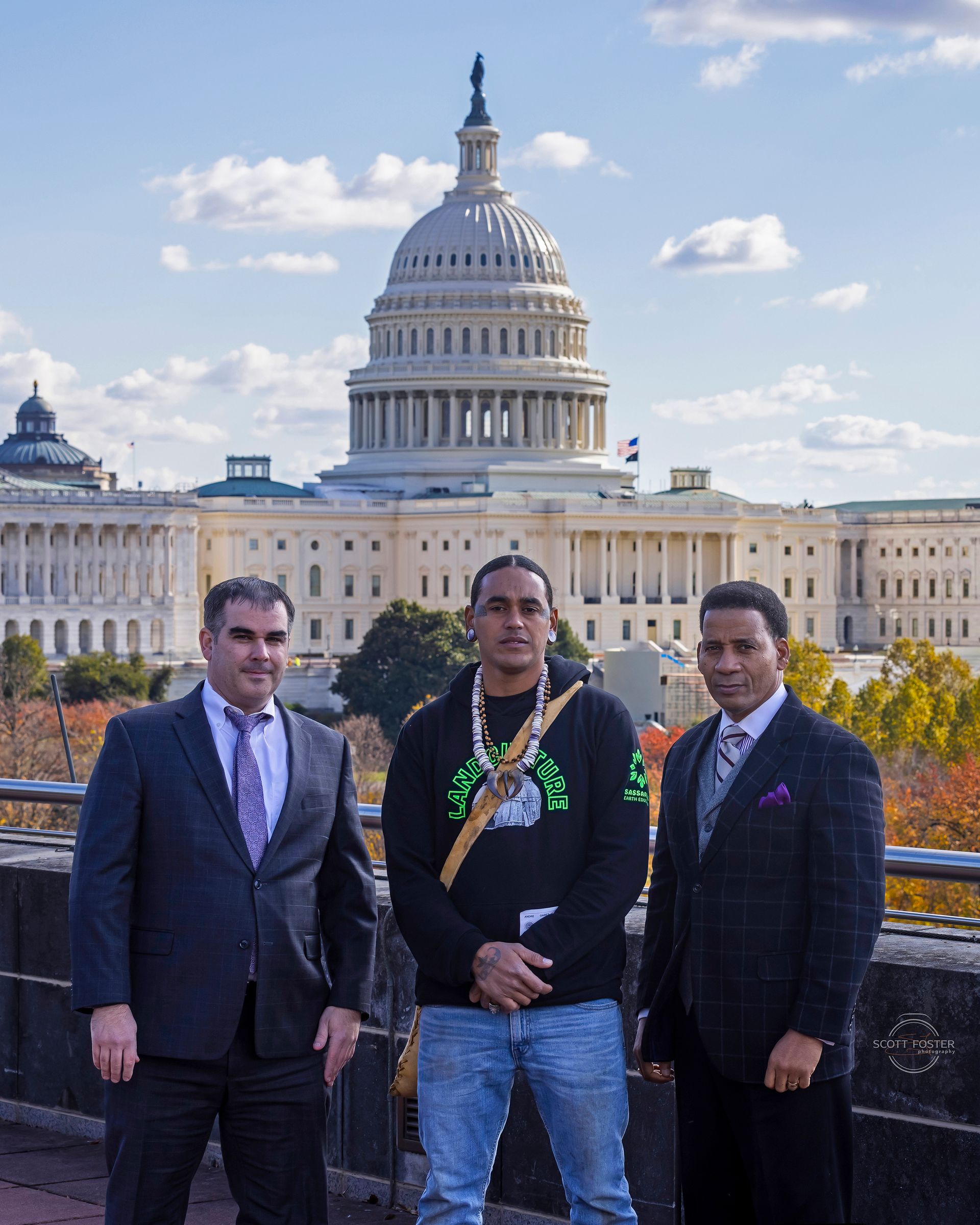 Three men pose in front of the U.S. Capitol building on a sunny day.
