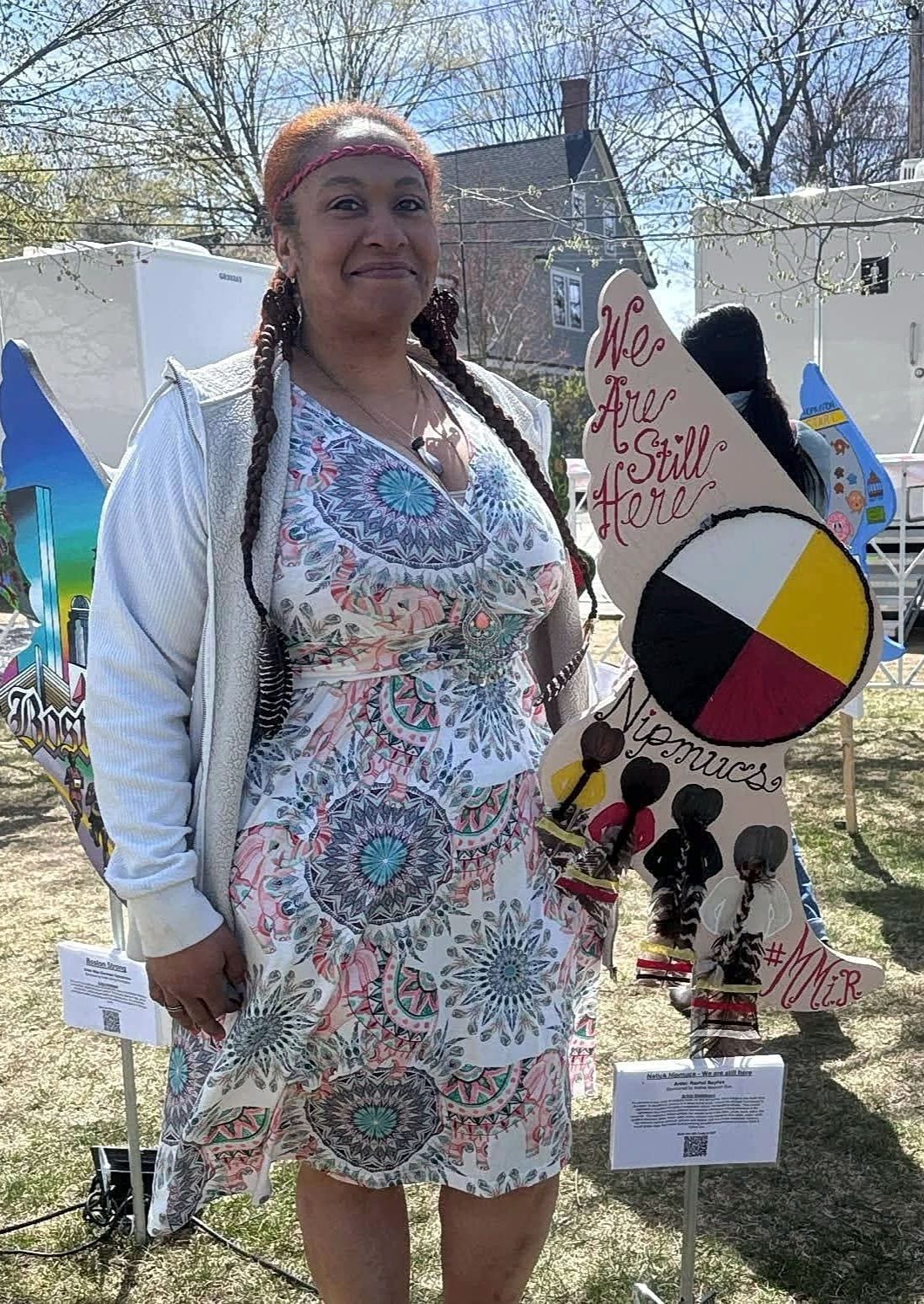 Woman in floral dress, poses near a Native American art piece in an outdoor setting.
