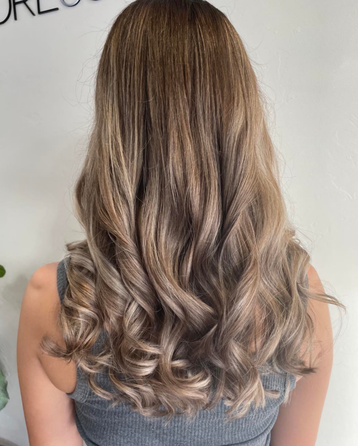 A Woman With Long Curly Hair is Wearing a Gray Tank Top — Hairdressers At Work in Cairns City, QLD