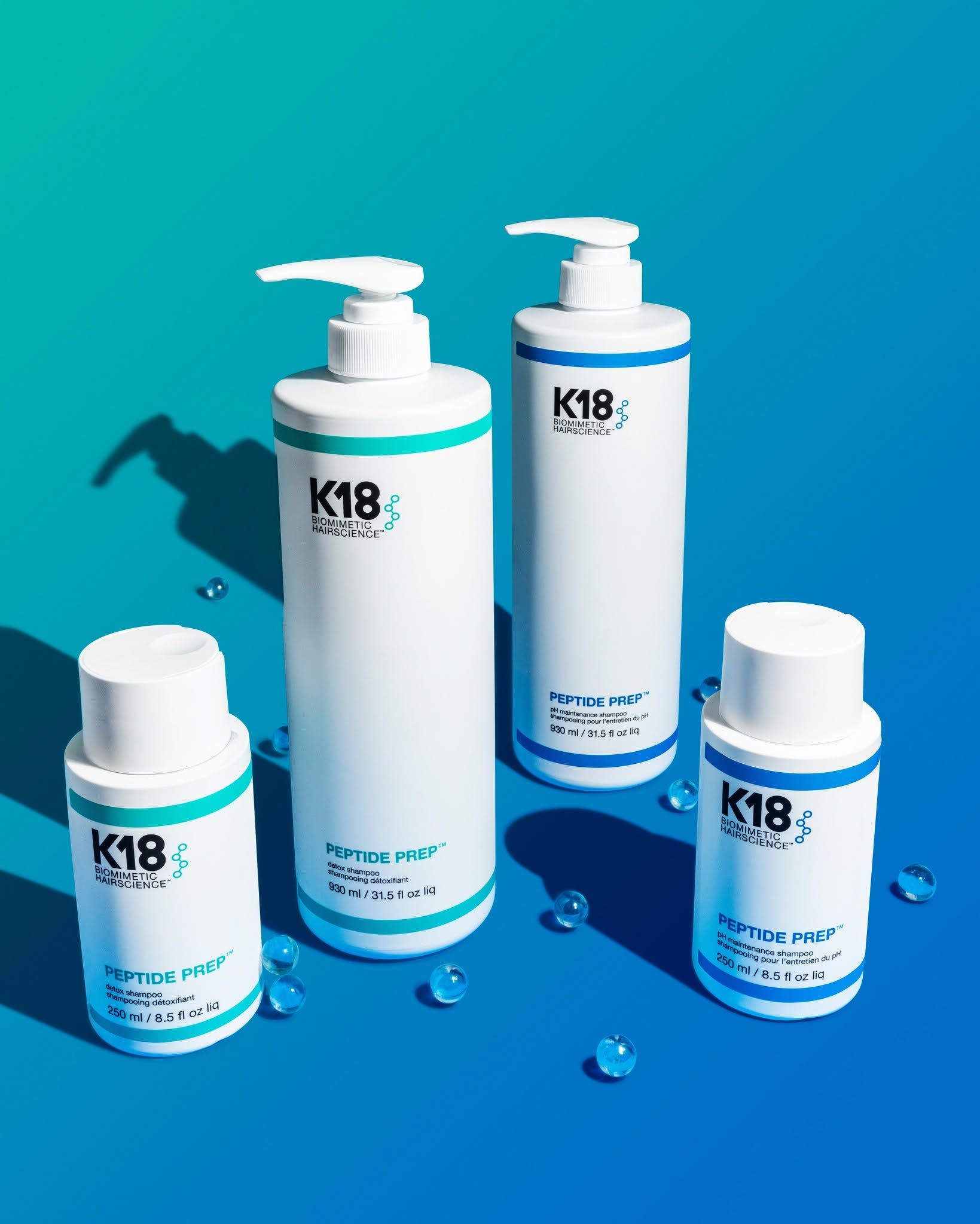 K18 haircare bottles on pink blocks against a rainbow gradient background
