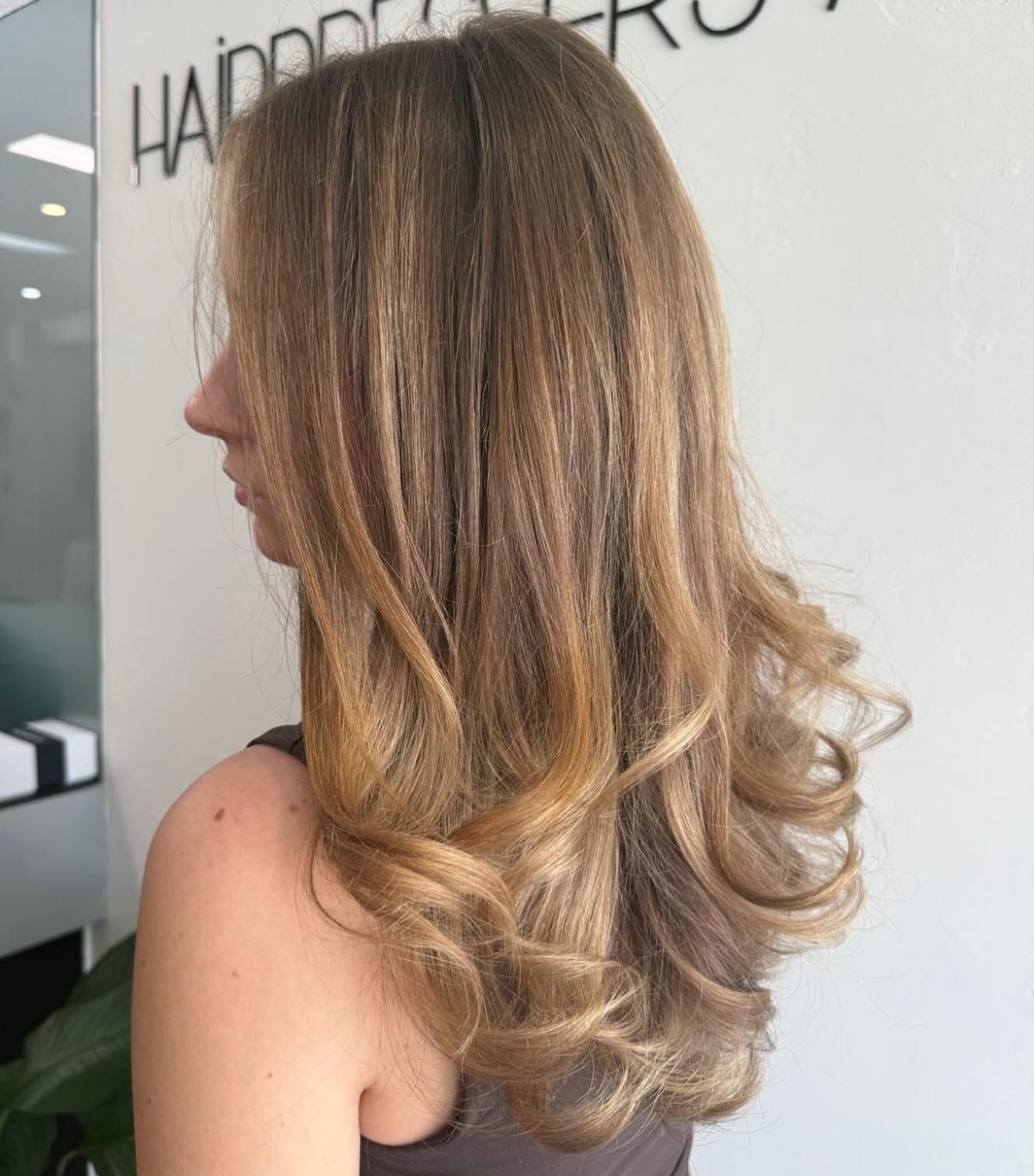 A Woman With Long Blonde Hair is Wearing a White Tank Top — Hairdresser At Work in Cairns City, QLD