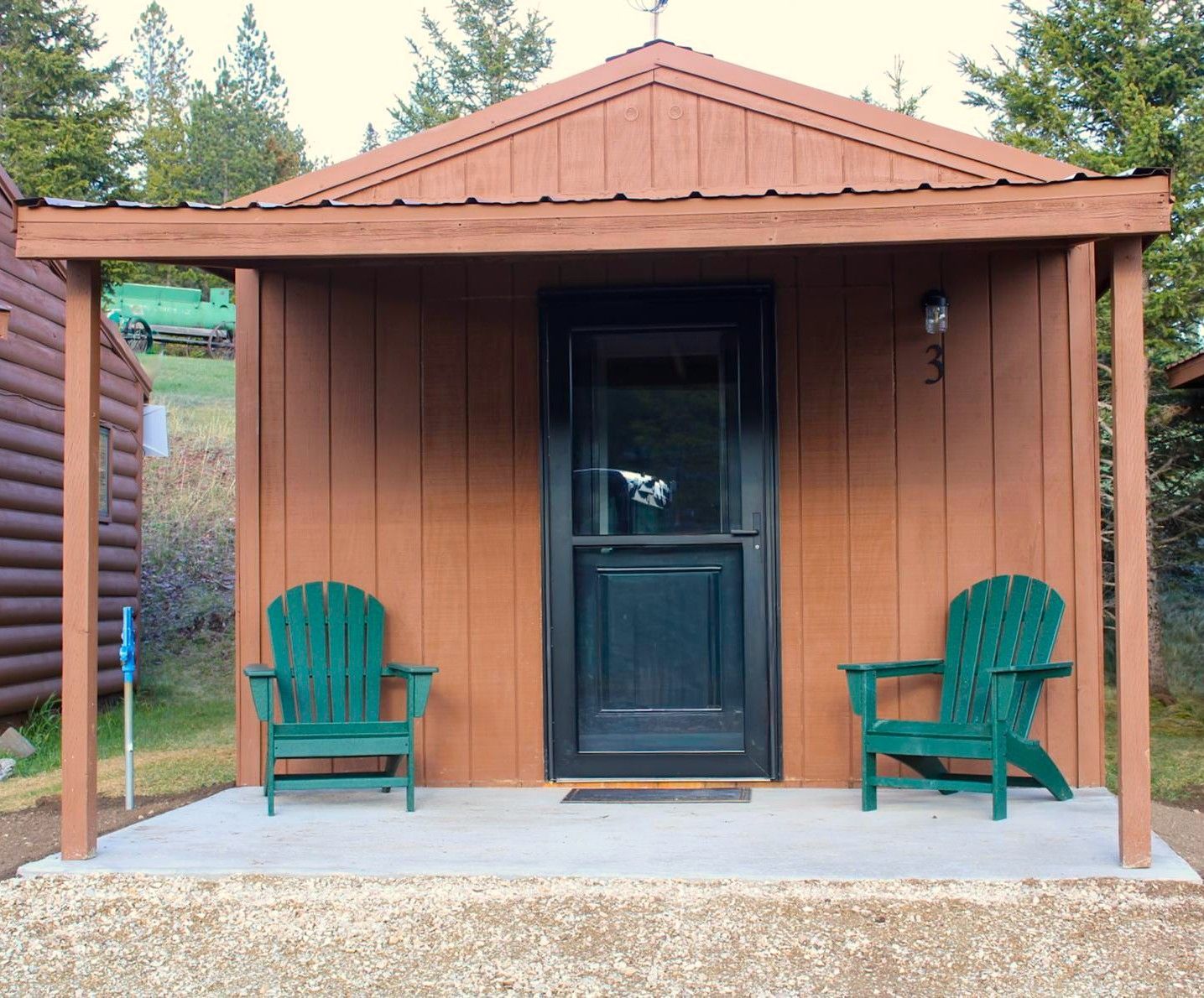 Small brown cabin porch with black door and two green chairs under a covered roof