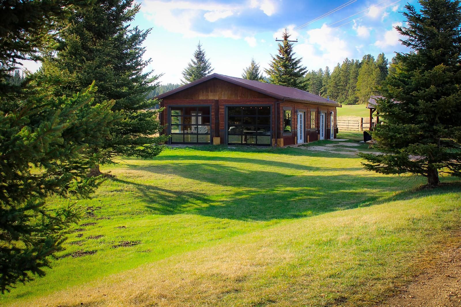 Wooden cabin in a sunny grassy clearing surrounded by evergreen trees