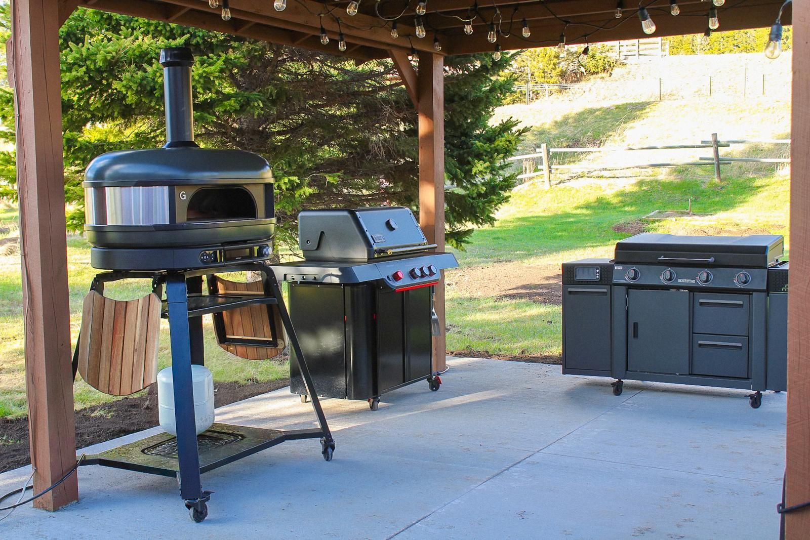 Outdoor patio with a black pellet grill, smoker, and a covered grill station under a wooden roof.