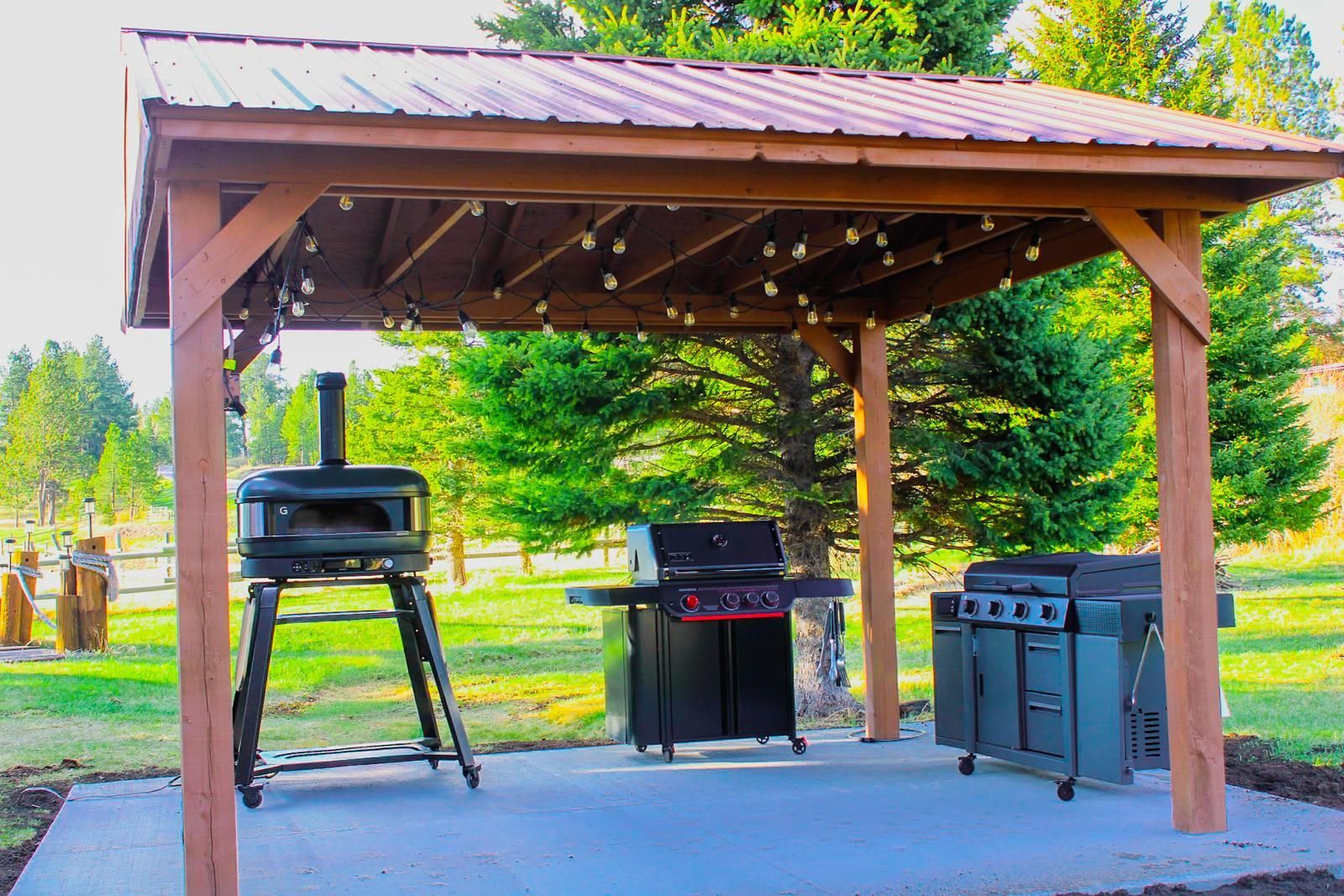 Covered outdoor patio with a grill, smoker, and black storage cabinets on a concrete slab.